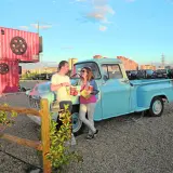 Pareja disfrutando de planes en pareja originales sin dinero en un autocine, apoyados en una camioneta azul, con palomitas y bebidas.