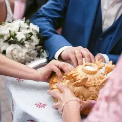 Manos de novios tocando un pan decorado, parte de rituales de boda en diferentes culturas.