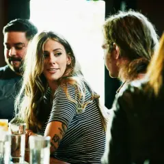 Una mujer sonríe mientras conversa en un bar, quizás aprendiendo como ligar.