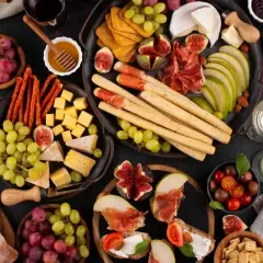 Un delicioso picoteo gourmet con quesos, embutidos, frutas, pan y vino.