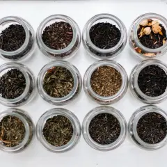 Doce frascos de vidrio muestran diferentes tipos de infusiones, desde tés negros hasta verdes y especiados.