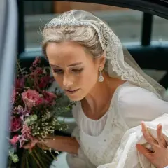 Novia con velo de encaje y pendientes largos, un ejemplo de las últimas tendencias en pendientes de novia. Lleva un ramo de rosas.