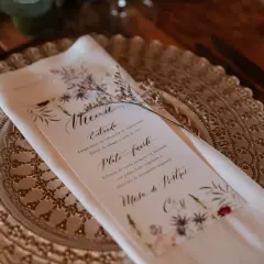 Un elegante menú de boda con caligrafía floral detalla los platos: langostinos, solomito de cerdo y mesa de postres.