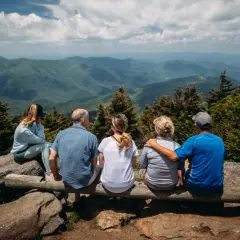 Cinco personas, representando distintas etapas de la vida, contemplan un vasto paisaje montañoso.