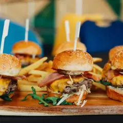 Picoteo comida para cumpleaños en casa: mini hamburguesas jugosas con queso fundido, tocino crujiente y papas fritas. ¡Un festín delicioso!