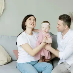 Parejas latinas con hijos, una familia feliz en el sofá. La madre mira hacia arriba con asombro, el padre sonríe a su bebé.