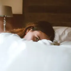 Una mujer yace en la cama, oculta entre las sábanas, con una mirada que evoca la disforia postcoital.