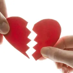 Manos separando un corazón rojo roto, símbolo del mal de amores.