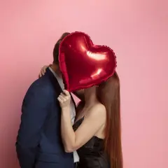 Pareja besándose detrás de un globo rojo en forma de corazón. Ideas románticas para sorprender a tu pareja.