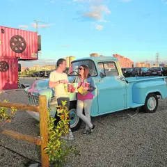 Pareja disfrutando de planes en pareja originales sin dinero en un autocine, apoyados en una camioneta azul, con palomitas y bebidas.