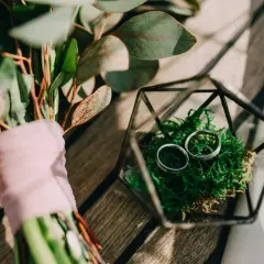 Anillos de boda en musgo dentro de un terrario de vidrio, junto a un ramo con flores y velo rosa. Celebrando un aniversario boda 5 años.