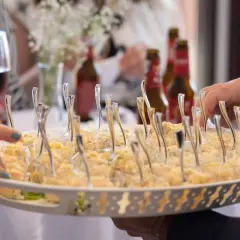 Bandeja con aperitivos individuales, ideal para un coctel de bienvenida de boda. Se ven manos tomando uno.