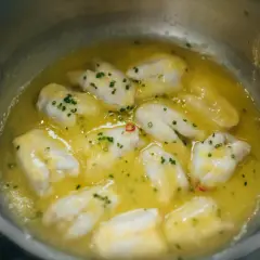 Trozos de bacalao cocinándose en aceite de oliva con ajo y guindilla, listos para la bacalao pil pil receta.