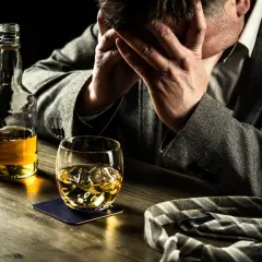 Hombre angustiado con botella y vaso de whisky. Busca remedios caseros para dejar de beber alcohol.