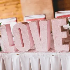 Letras gigantes "LOVE" en rosa brillante, un detalle perfecto para una decoración boda civil sencilla y barata. Flores a los lados.