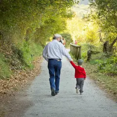 Abuelo y nieto caminan de la mano por un sendero otoñal. Un ejemplo de refranes cortos: "La unión hace la fuerza".