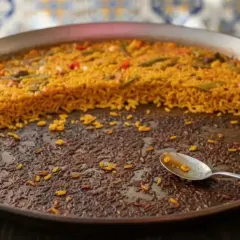 Paella casi terminada en una paellera. El arroz pegado en el fondo, con una cuchara, indica que ha sido deliciosa.