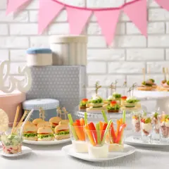 Mesa de baby shower con deliciosa comida: mini hamburguesas, canapés, palitos de verduras con dip y vasitos de aperitivos.