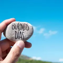Un cariñoso saludo de buenos días alegres, escrito en una piedra sostenida contra un cielo azul brillante.
