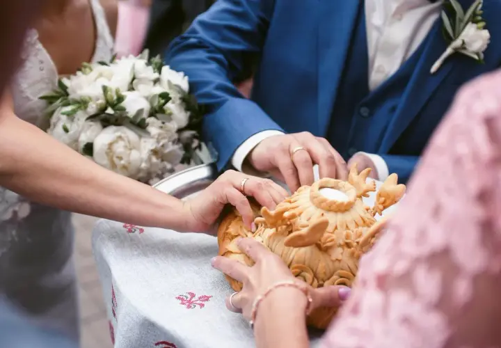 Manos de novios tocando un pan decorado, parte de rituales de boda en diferentes culturas.