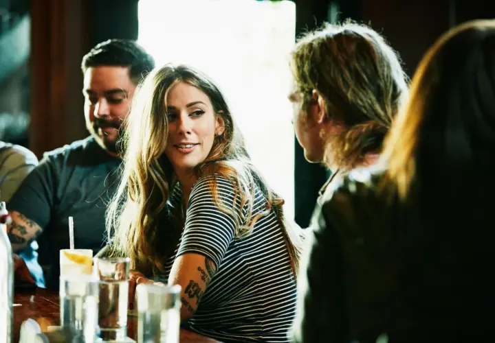 Una mujer sonríe mientras conversa en un bar, quizás aprendiendo como ligar.