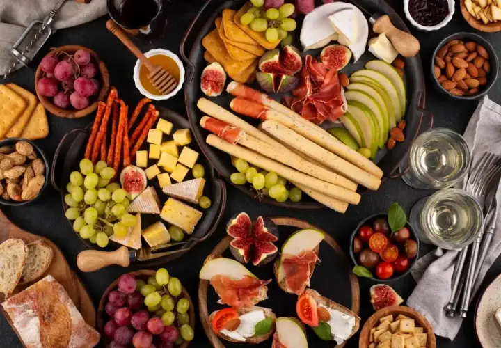 Un delicioso picoteo gourmet con quesos, embutidos, frutas, pan y vino.