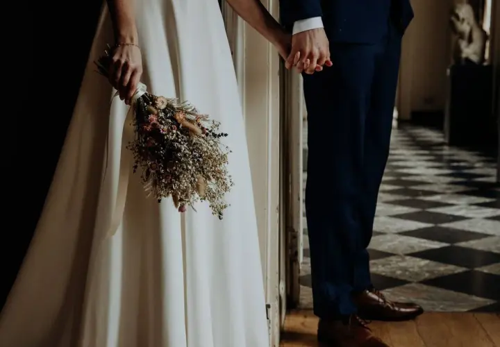Novios tomados de la mano, ella con un ramo de flores secas, listos para su ceremonia civil.