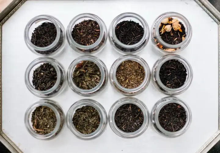 Doce frascos de vidrio muestran diferentes tipos de infusiones, desde tés negros hasta verdes y especiados.
