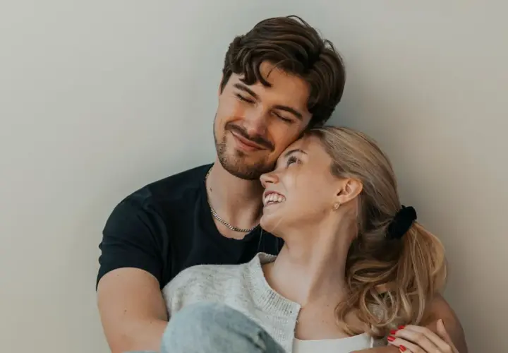 Una pareja joven se abraza tiernamente, sus rostros iluminados por una sonrisa que refleja el amor verdadero.
