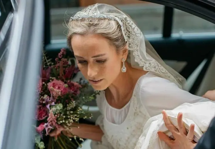 Novia con velo de encaje y pendientes largos, un ejemplo de las últimas tendencias en pendientes de novia. Lleva un ramo de rosas.
