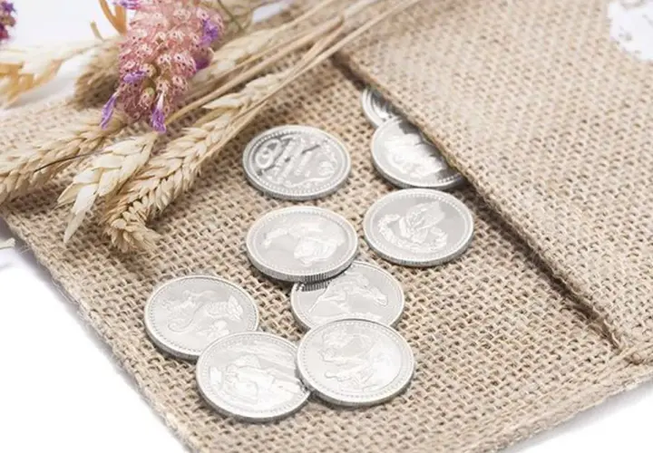 Monedas plateadas, símbolo de prosperidad, junto a espigas y flores secas, representando las arras de boda.