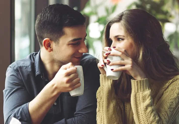 Una pareja joven comparte un café, mirándose con ternura. Un momento perfecto para pensar como decirle a alguien que te gusta.
