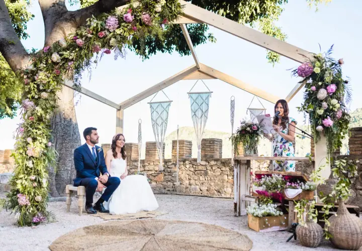 Novia y novio sentados, oficiante leyendo. La decoración floral es exuberante. ¿Cuánto dura una boda civil? Depende de la ceremonia.