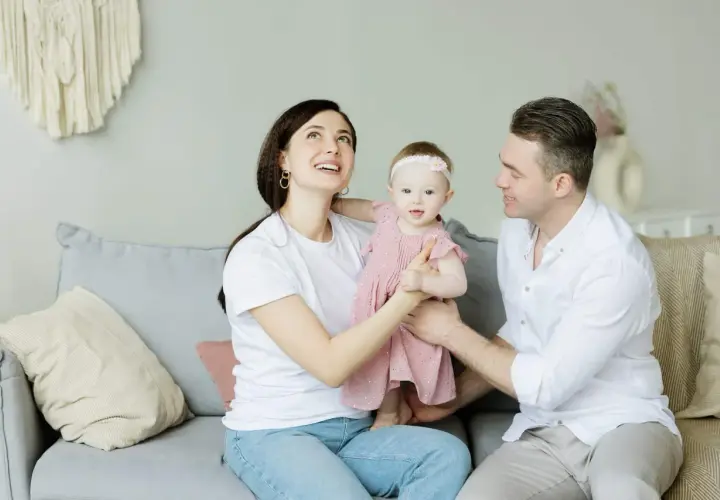 Parejas latinas con hijos, una familia feliz en el sofá. La madre mira hacia arriba con asombro, el padre sonríe a su bebé.
