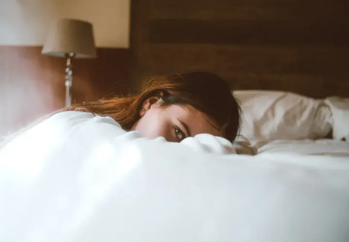Una mujer yace en la cama, oculta entre las sábanas, con una mirada que evoca la disforia postcoital.