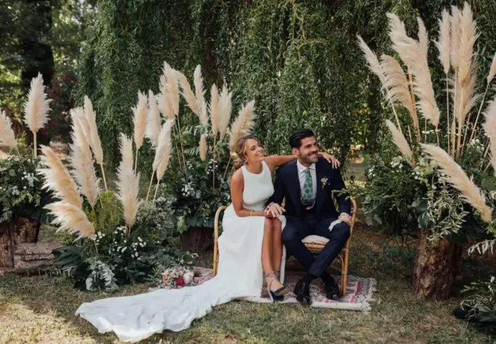 Novios sonriendo en su **boda del año**, rodeados de pampas y vegetación exuberante.