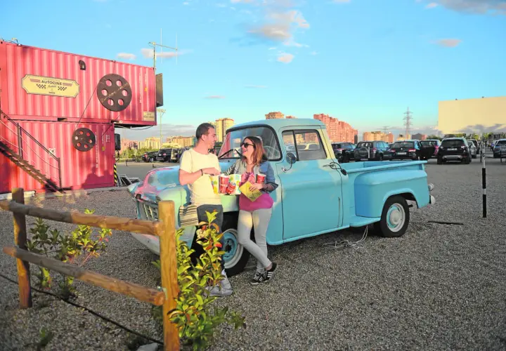 Pareja disfrutando de planes en pareja originales sin dinero en un autocine, apoyados en una camioneta azul, con palomitas y bebidas.