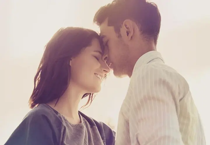 Parejas enamoradas, con sus frentes juntas y sonrisas tiernas, bajo la luz cálida del atardecer.