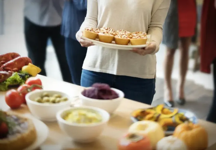 Una mujer lleva una bandeja de pastelitos para una merienda de cumpleaños para adultos. Hay langosta, tomates y otros aperitivos en la mesa.