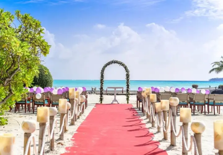 Alfombra roja y sillas decoradas con globos para una hermosa ceremonia de boda en la playa. El mar turquesa y el cielo azul crean el escenario perfecto.