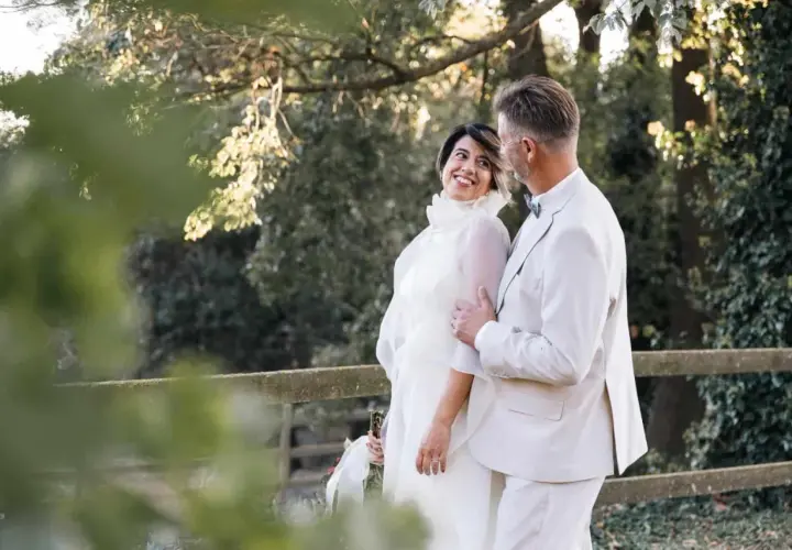 Pareja sonriente en su segunda boda a los 50 años de edad. Ella luce un vestido blanco vaporoso, él un traje claro.