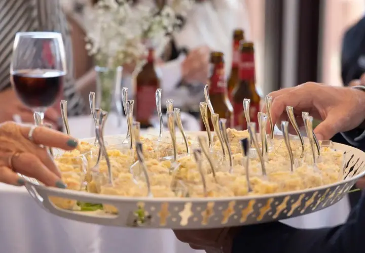 Bandeja con aperitivos individuales, ideal para un coctel de bienvenida de boda. Se ven manos tomando uno.