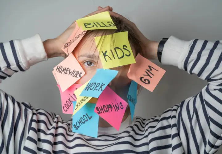 Una persona agobiada por notas adhesivas con tareas: "Kids", "Bills", "Homework", "Work", "Shopping", "Gym", "School", "Groceries", "Cleaning". Un recordatorio visual de cómo ser mejor persona es priorizar.