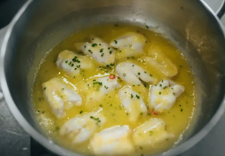 Trozos de bacalao cocinándose en aceite de oliva con ajo y guindilla, listos para la bacalao pil pil receta.