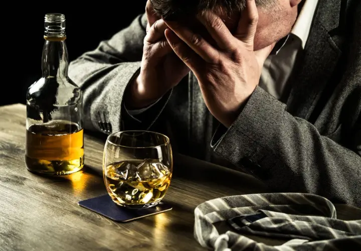 Hombre angustiado con botella y vaso de whisky. Busca remedios caseros para dejar de beber alcohol.