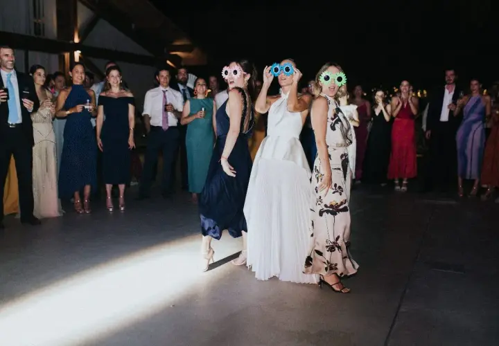 Un grupo de mujeres con gafas divertidas celebra una sorpresa para los novios en una fiesta.