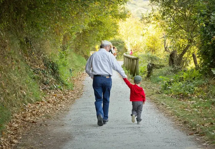Abuelo y nieto caminan de la mano por un sendero otoñal. Un ejemplo de refranes cortos: "La unión hace la fuerza".