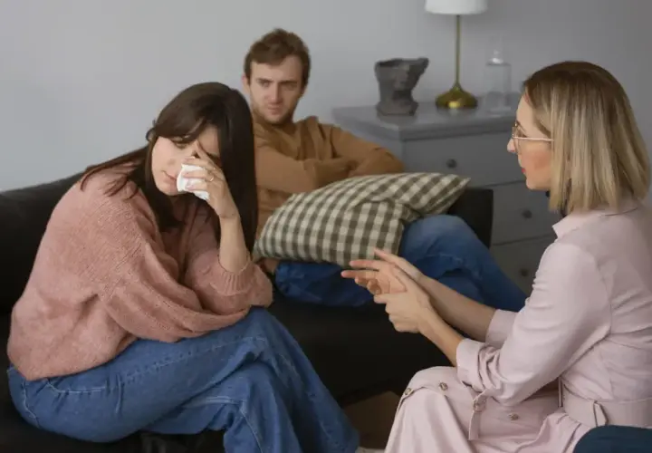 Una pareja discute temas de conversación difíciles con un terapeuta. La mujer llora mientras el hombre la mira.