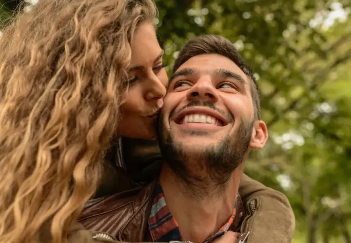 Una mujer rubia besa en la mejilla a un hombre sonriente. Las reglas de pareja se basan en el amor y la confianza.