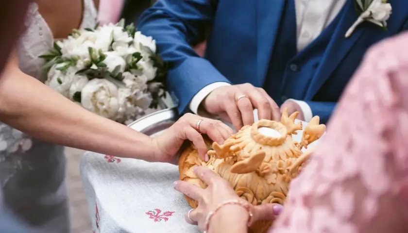 Manos de novios tocando un pan decorado, parte de rituales de boda en diferentes culturas.